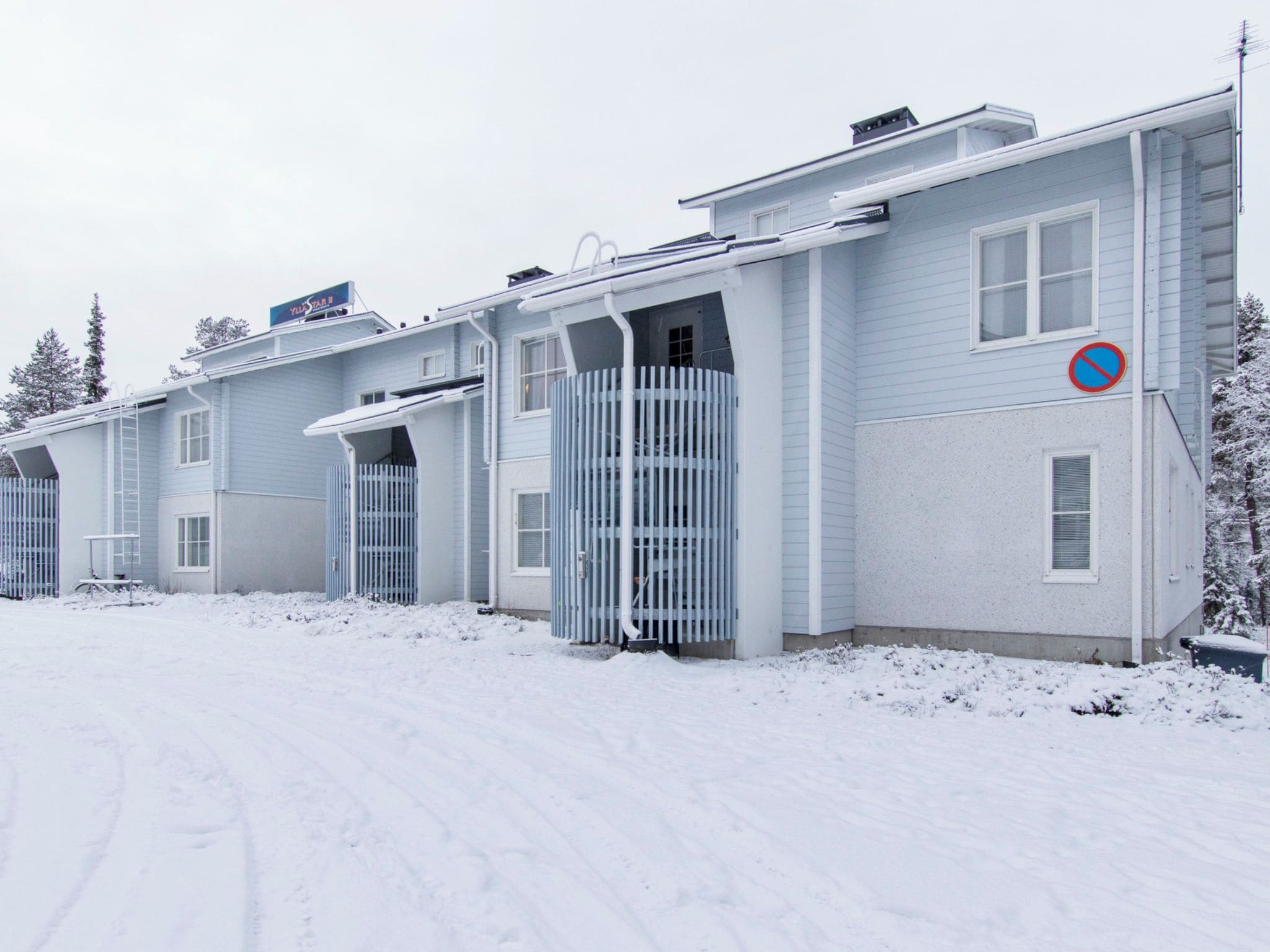 Eine Reihe hellblauer Gebäude, mit einem Verbotsschild, einem befestigten Eingang und einem mit Schnee bedeckten Untergrund.