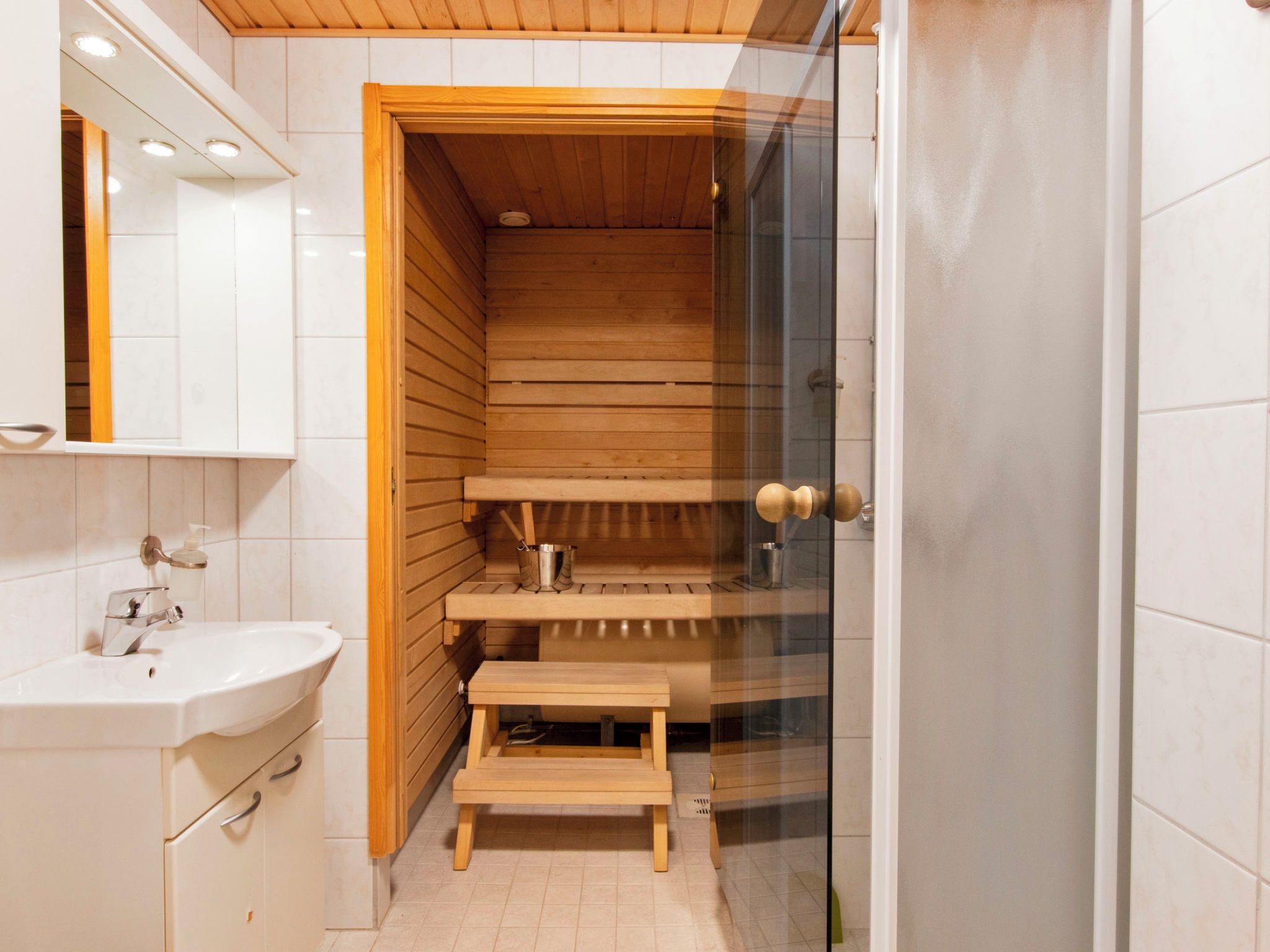 Ein modernes Badezimmer mit einer Holzsauna, einer Duschkabine aus Glas und einem weißen Waschbecken.