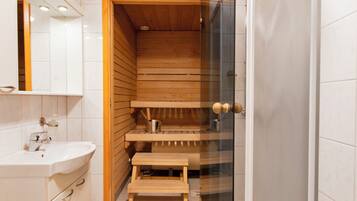 Ein modernes Badezimmer mit einer Holzsauna, einer Duschkabine aus Glas und einem weißen Waschbecken.