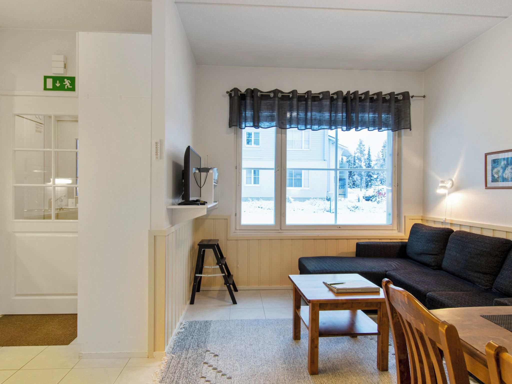 Ein Zimmer mit einer Couch, einem Tisch, einem Fernseher und einem Fenster mit Blick auf eine verschneite Landschaft.