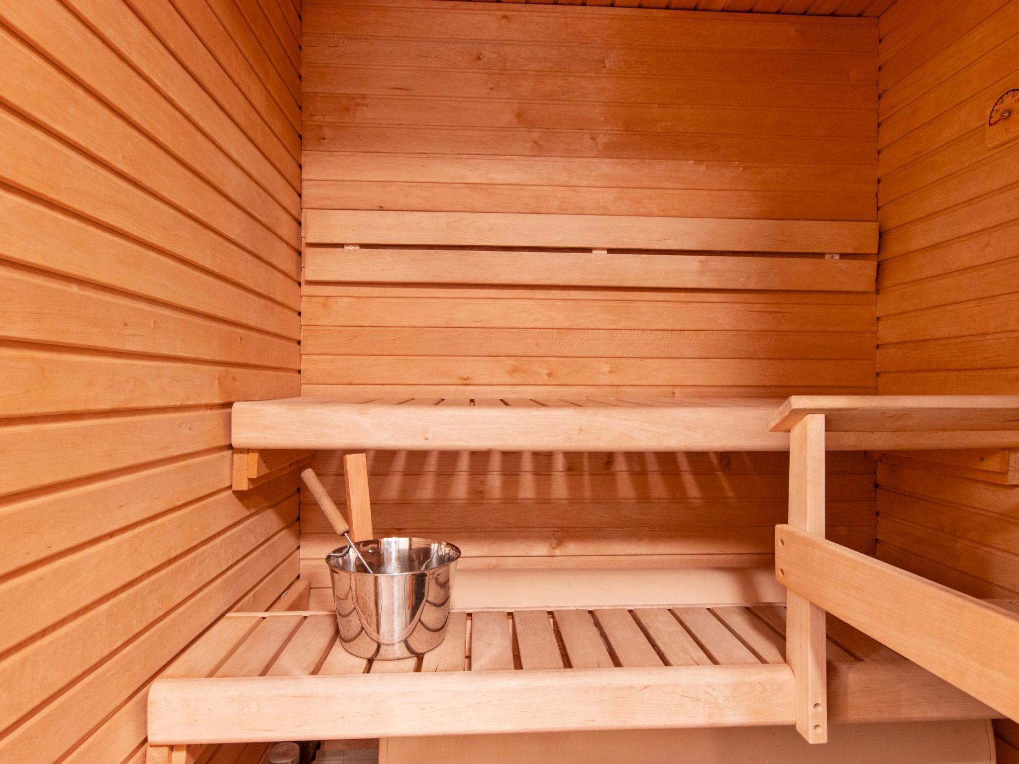 A wooden sauna with a metal bucket on the lower shelf.
