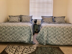 A bedroom with two beds, a patterned rug, and a window with blinds.