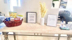 A room with a table displaying snacks, a welcome home sign, a house manual, and a bottle of hand sanitizer. - Chateau Saguaro is your home away from home (La Quinta)