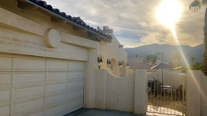 A garage with a white door, a concrete patio, and a gate leading to a seating area with tables and chairs. - Chateau Saguaro is your home away from home (La Quinta)