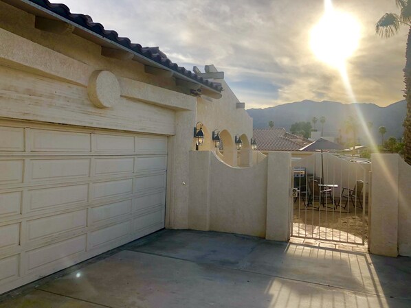 A garage with a white door, a concrete patio, and a gate leading to a seating area with tables and chairs.