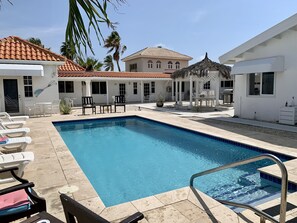 Piscina com espreguiçadeiras e área de estar coberta.