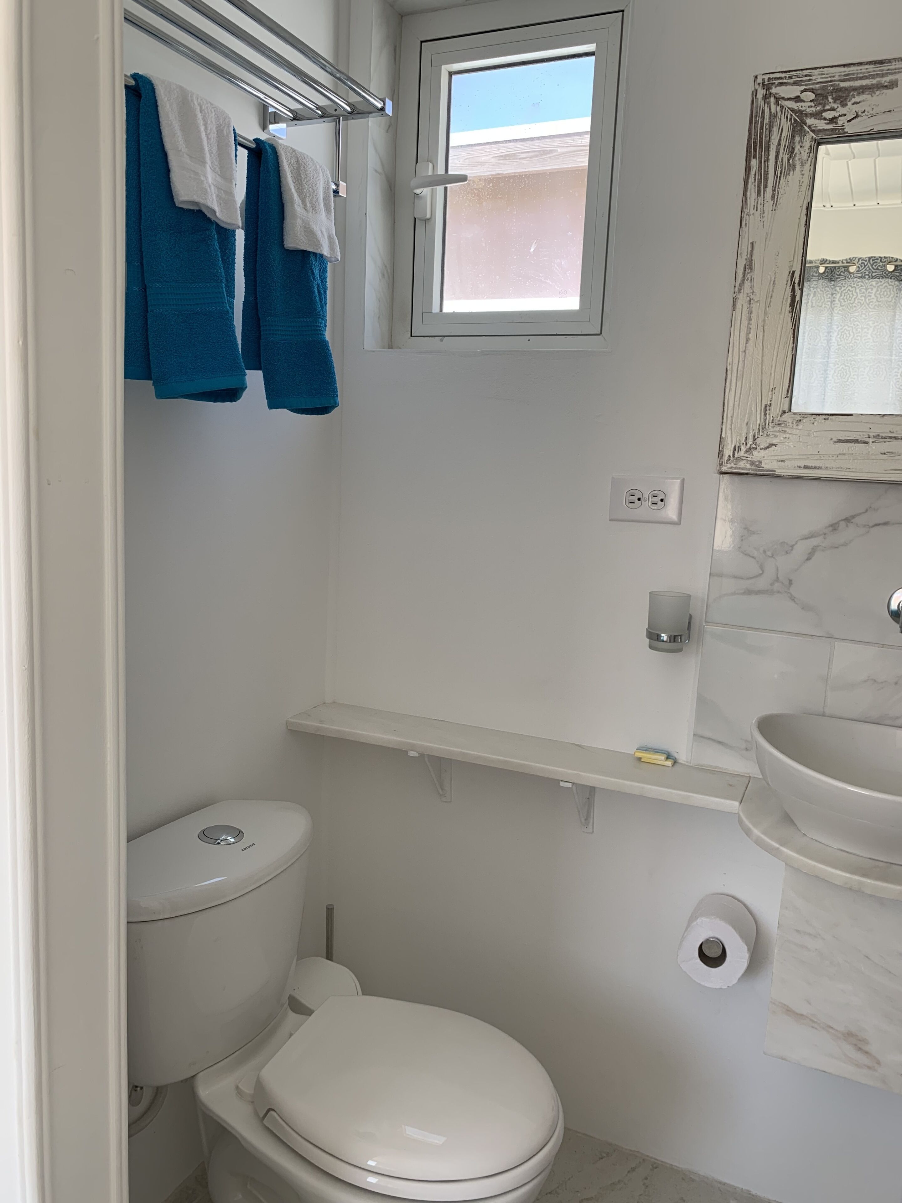 Een compacte badkamer met toilet, een klein raam, een wastafel en een handdoekrek met blauwe handdoeken.