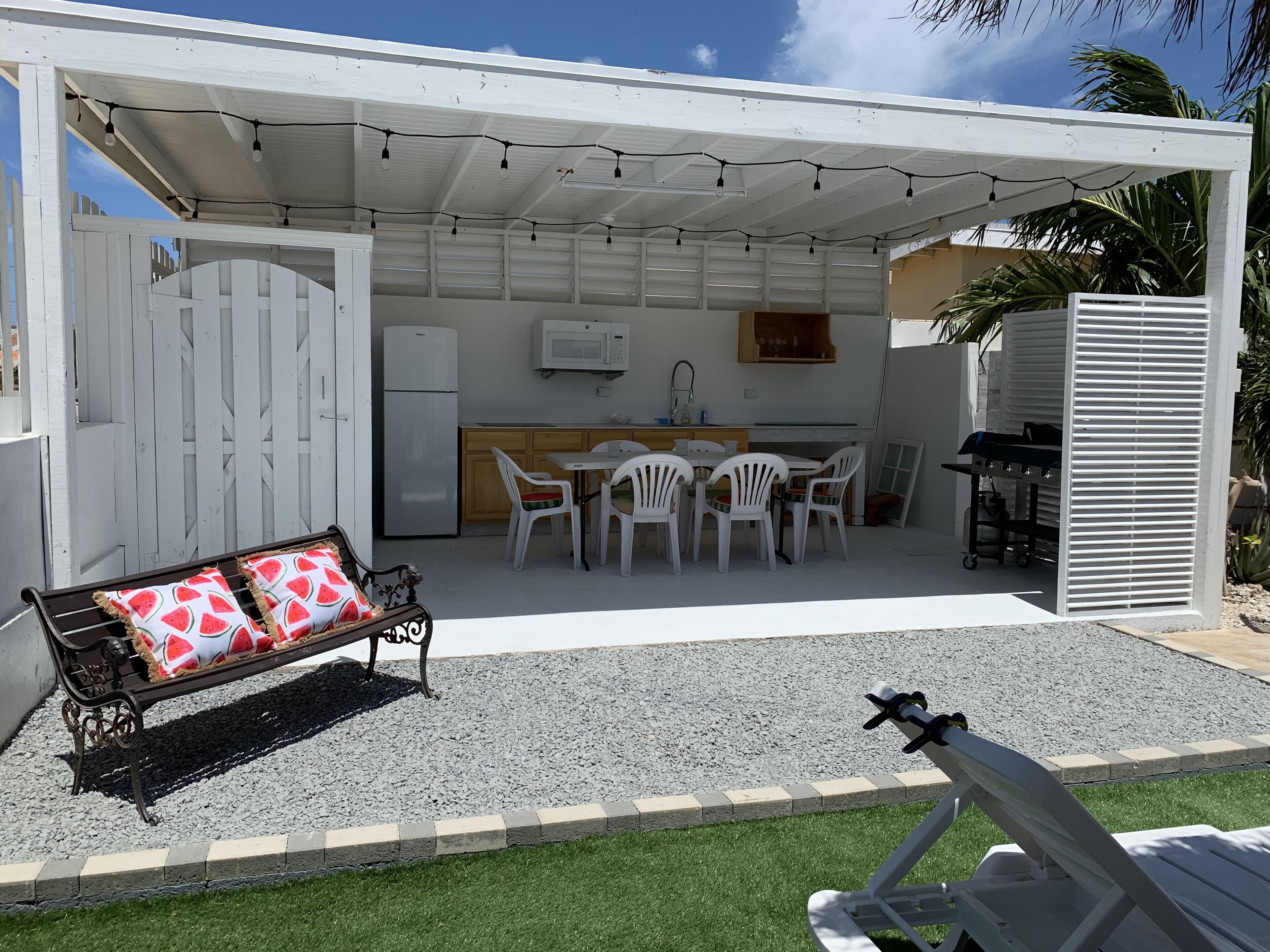 A covered outdoor patio with a dining area, a grill, and a refrigerator.