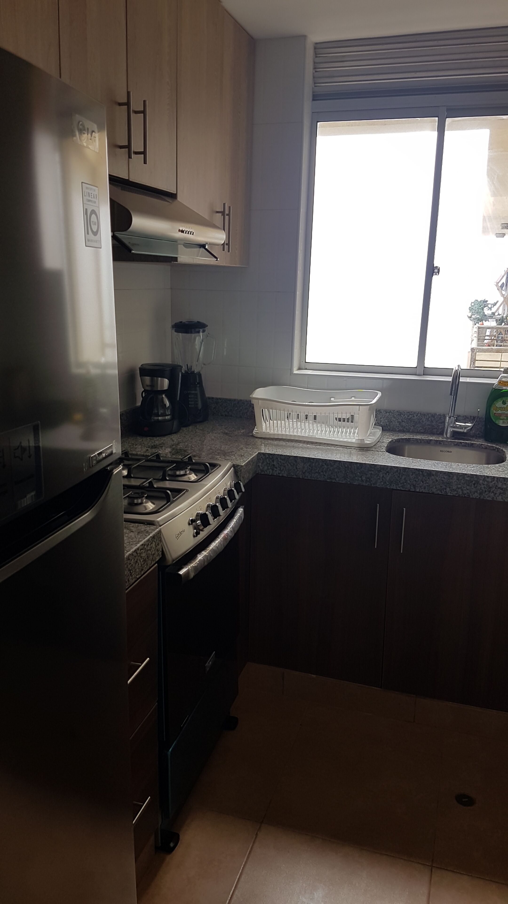A kitchen with a refrigerator, stove, coffee maker, and a window with blinds.