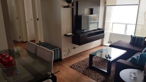A modern living room with a glass coffee table, a sofa, a TV mounted on the wall, and a fireplace. - LIMA FLAT 5 2D BETWEEN AIRPORT AND MIRAFLORES (San Miguel)