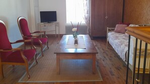 Una sala de estar con televisor, un mueble de madera, un sofá y una mesa de centro.