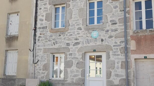 Un edificio de piedra con una puerta blanca, dos ventanas y un pequeño letrero sobre la puerta.