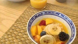 Una mesa de desayuno con tostadas, un vaso de jugo de naranja, un tazón de fruta, un frasco de mermelada y una taza de leche.