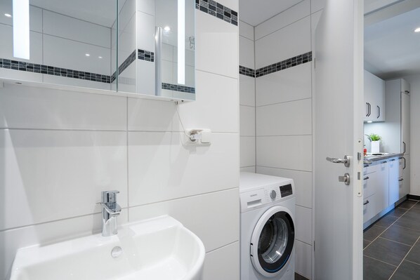 Une salle de bain moderne avec un lavabo blanc, un lave-linge et un miroir.