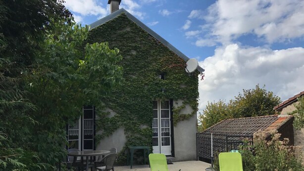 Ein Haus mit Efeu bewachsener Mauer, einer Satellitenschüssel und einer Terrasse mit zwei grünen Liegestühlen.
