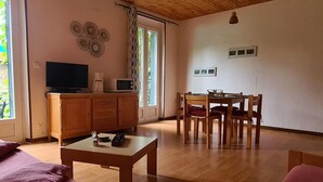 Ein gemütliches Wohnzimmer mit Holzbalkendecke, einem Essbereich mit Tisch und Stühlen, einem Fernseher auf einer Anrichte und einem Fenster mit Vorhängen.