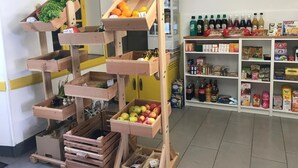 Ein hölzerner Obststand mit Äpfeln und Orangen, und eine Ablage mit verschiedenen Getränken und Snacks.