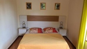 Ein ordentlich bezogenes Bett mit einer beigen Tagesdecke und zwei Kissen, das von beiden Seiten Nachttische mit Lampen säumt.
