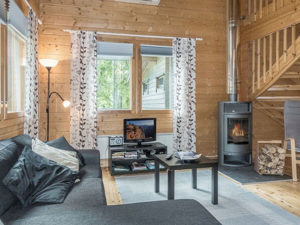 A cozy cabin interior with a sofa, television, and wood-burning stove.