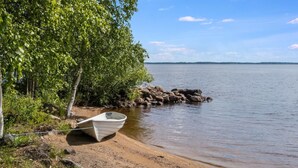 A boat on a sandy beach with trees and rocks nearby.