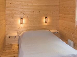 A single bed with a white mattress in a wooden cabin room.