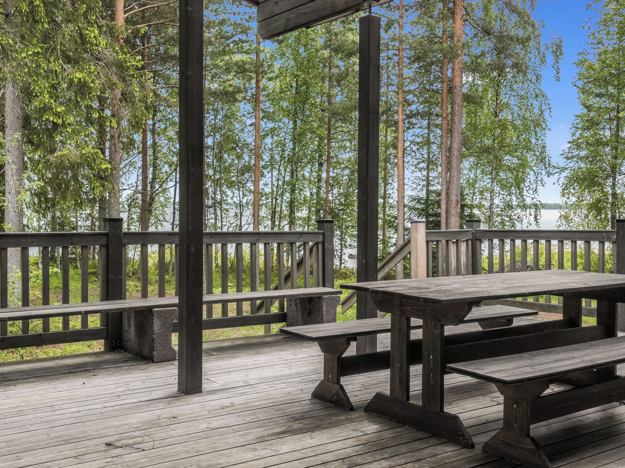 A wooden deck with picnic tables and a railing overlooking a forested area.
