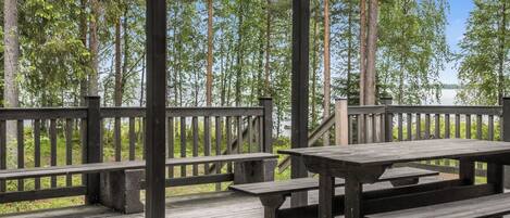 A wooden deck with picnic tables and a railing overlooking a forested area.