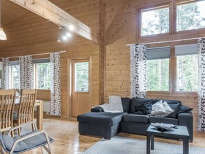 A wooden cabin interior with a sofa, chairs, a table, and large windows.