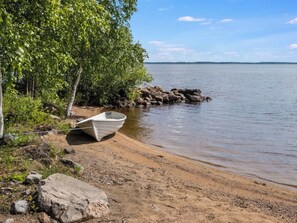 Un bateau sur une plage de sable, au bord d’un lac paisible, entouré d’arbres et de rochers.