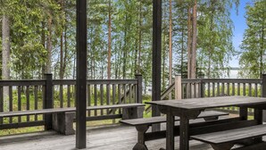 A wooden deck with picnic tables and a railing overlooking a forested area.