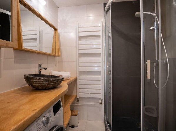 A modern bathroom with a wooden vanity, a stone basin sink, a built-in washing machine, a glass shower enclosure, and a white towel rack. - Le Curling B (Val Claret) by Interhome (Tignes)