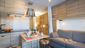 A modern kitchen with wooden cabinets, a dining table with chairs, and a grey sofa in a living area. - Le Curling B (Val Claret) by Interhome (Tignes)