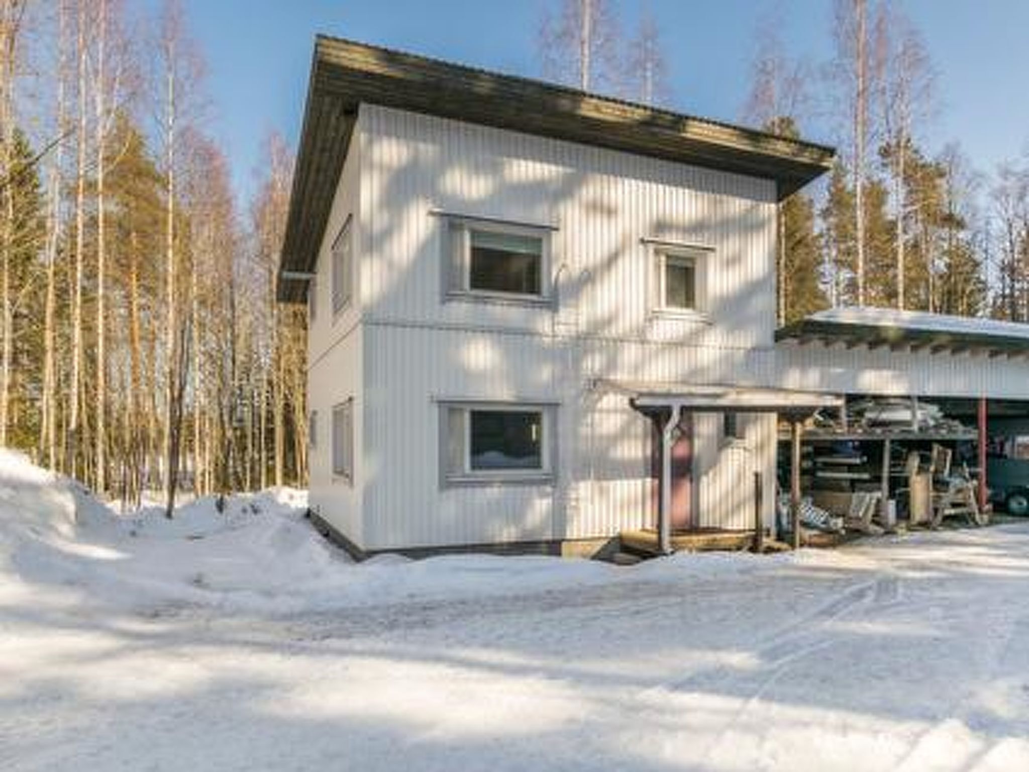 Kaksikerroksinen rakennus, jonka ulkoseinät ovat metallia, siinä on katettu kuisti ja autotalli, jossa on säilytettynä erilaisia tavaroita.