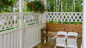 A wooden deck with a white lattice fence, a wooden bench, and two white plastic chairs.