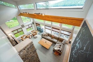 A spacious living area with a high ceiling, large windows, and a stone fireplace. - Sunlit Lakefront w/ Dock, Game Room & Firepit (Oakland)