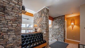 A stone wall, a black leather sofa, and a lamp in a room.