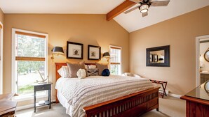 A bedroom with a large bed, a ceiling fan, a window with blinds, and a bedside table.