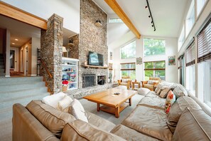 A spacious living room with a stone fireplace, a television, and comfortable seating. - Sunlit Lakefront w/ Dock, Game Room & Firepit (Oakland)