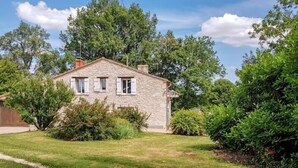 A stone house with a sloped roof, surrounded by a well-maintained lawn and dense greenery.