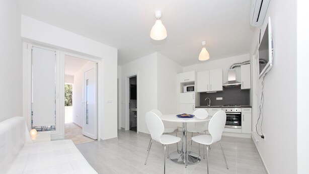 A modern kitchen with white cabinets, a microwave, and a stove. There is a dining table with four chairs. - One bedroom Lux apartment Rea (Bibinje)