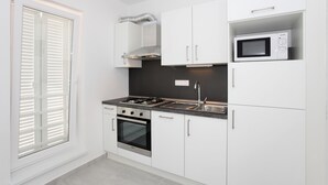 A modern kitchen with white cabinets, a built-in microwave, a gas stove, and a window with blinds. - One bedroom Lux apartment Rea (Bibinje)