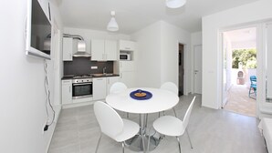 A modern kitchen with white cabinets, a built-in oven, and a microwave. There is a dining table with four chairs and a blue tray on it. - One bedroom Lux apartment Rea (Bibinje)