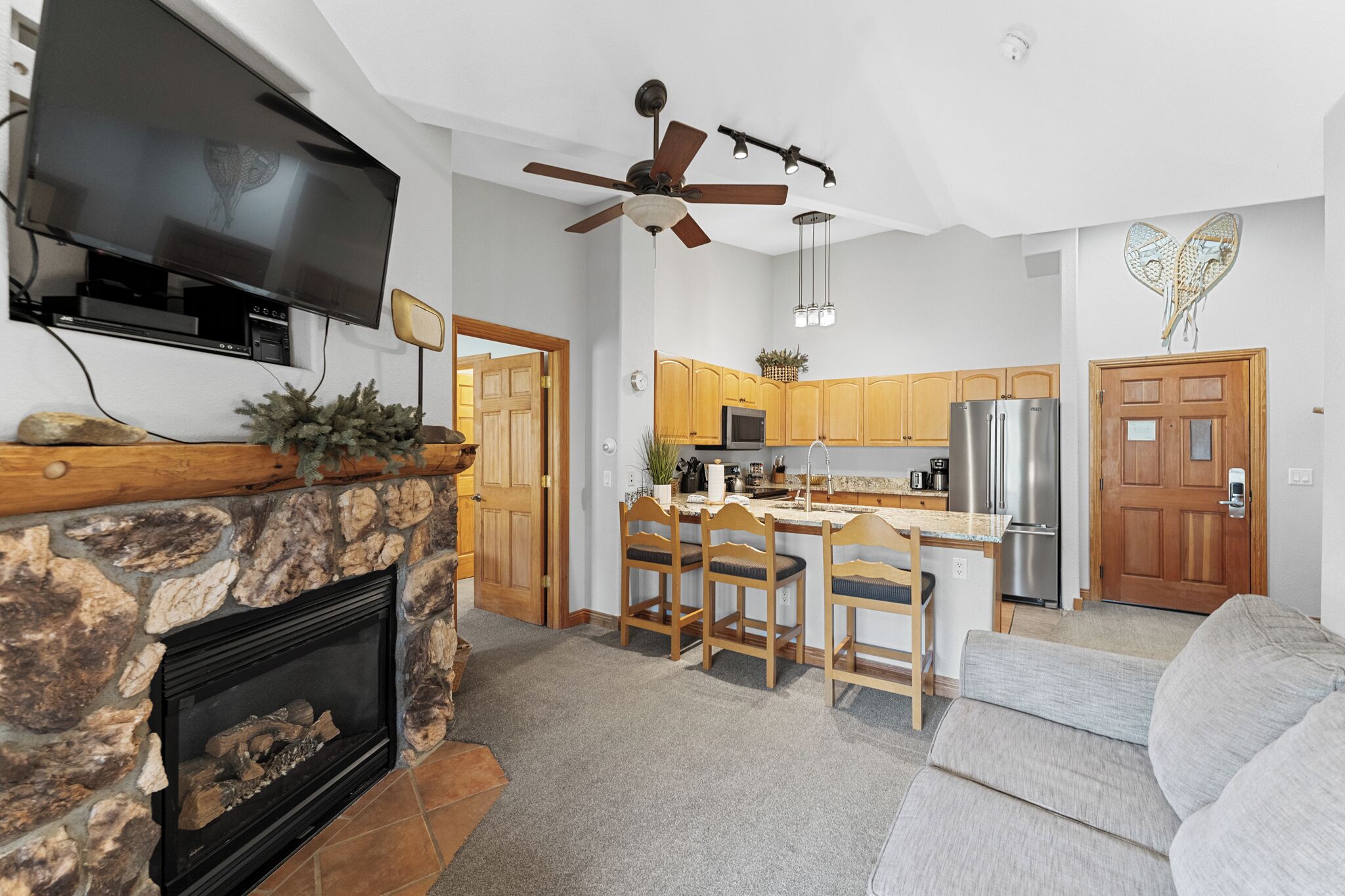 A modern kitchen with wooden cabinets, a stone fireplace, and a ceiling fan.