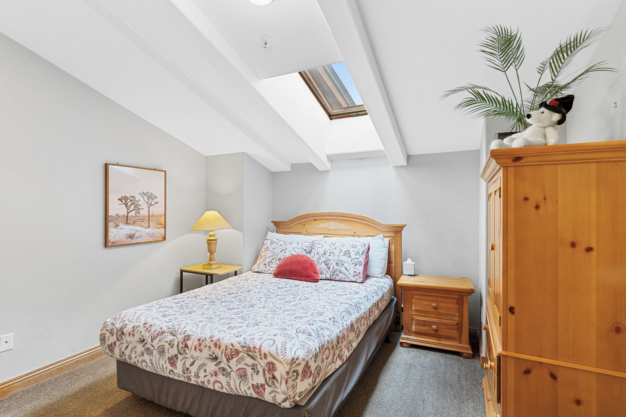 Une chambre à coucher avec un lit, une table de chevet, une lampe, une armoire, une plante et un puits de lumière.