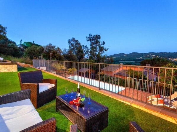 A terrace with wicker furniture, a pool, and a view of the countryside.