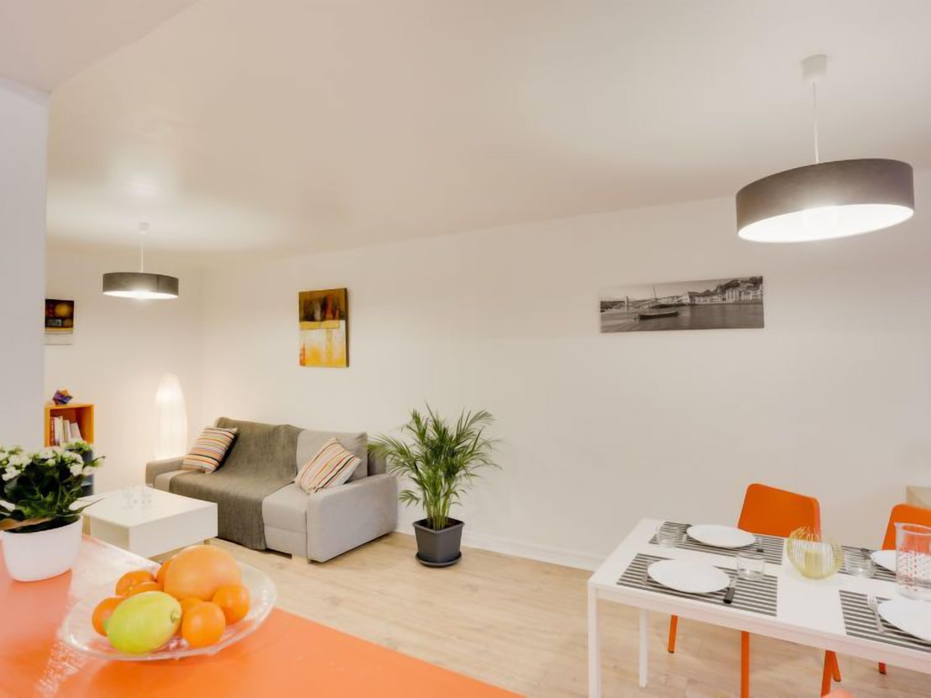 Ein modernes Wohnzimmer mit einem grauen Sofa, einem Esstisch gedeckt mit Tellern und Gläsern sowie einer Zimmerpflanze.