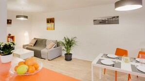 Una sala de estar moderna con un sofá gris, una mesa de comedor con platos y vasos, y una planta en maceta.