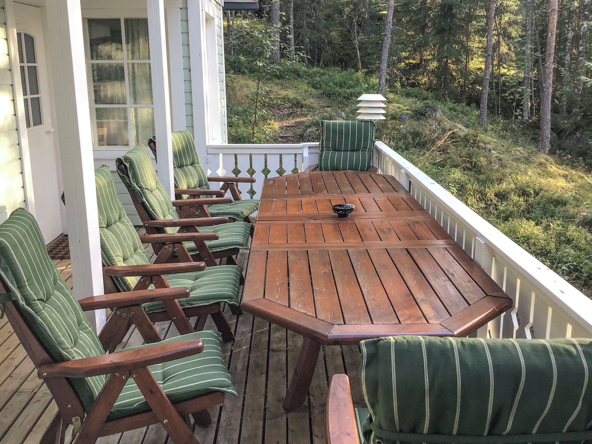 A wooden deck with a table and chairs, surrounded by a white railing, overlooking a forested area.