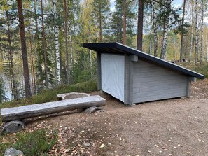 Une petite cabane en bois, dotée d’un toit en pente, située dans une zone boisée au sol recouvert de gravier.