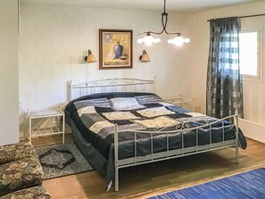 Un dormitori amb estructura de metall per al llit, una taula de nit, una làmpada, un quadre al mur i una finestra amb cortines.